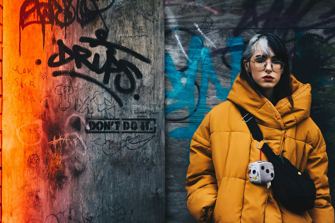 Person wearing a yellow coat by dolce vio standing in front of a graffiti-covered wall
