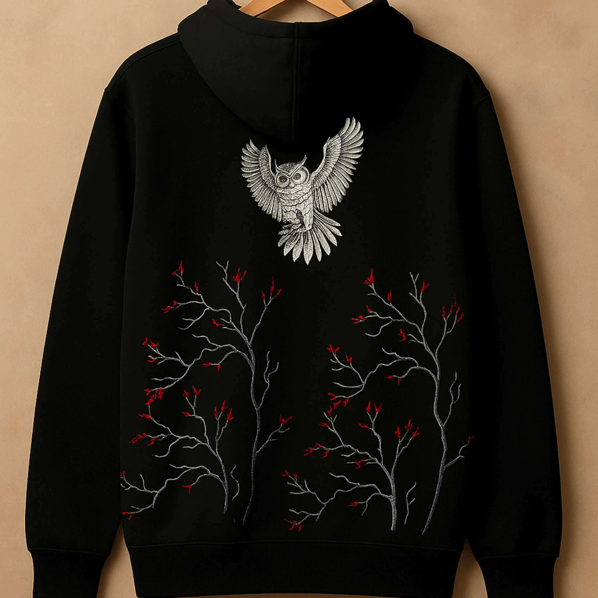 Black hoodie with an owl design on the back against a beige background